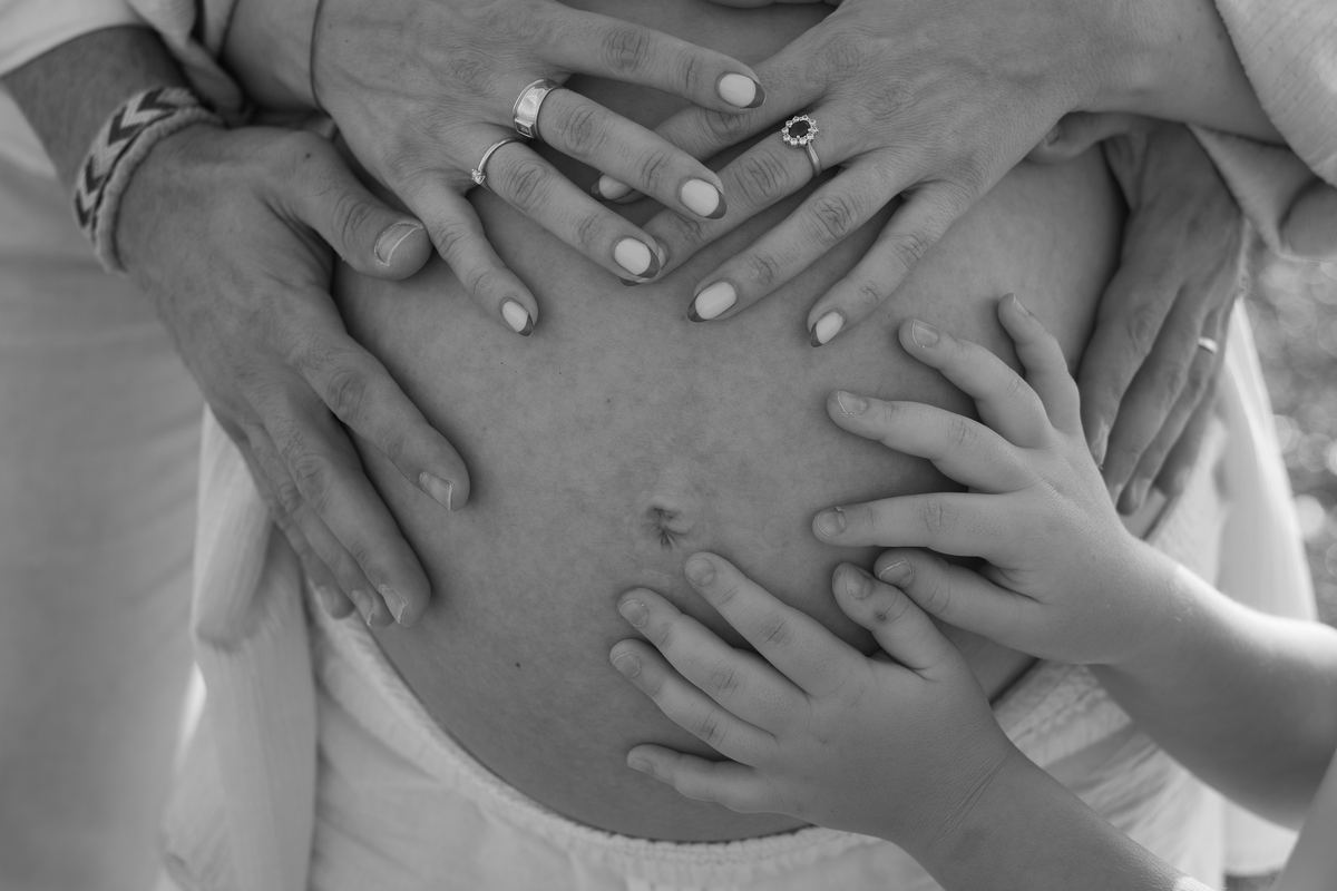 Manos de familiares sobre el vientre de embarazada
