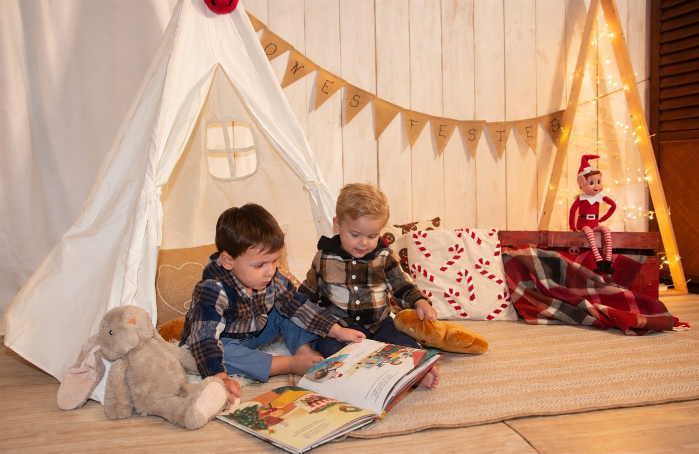 Dos hermanos leyendo un cuento dentro del rincón navideño del tipi