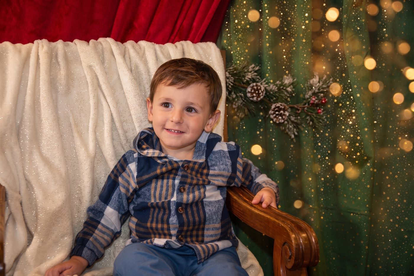 Niño sentado en un sillón de madera ante cortinas de terciopelo rojo y verde con estrellas