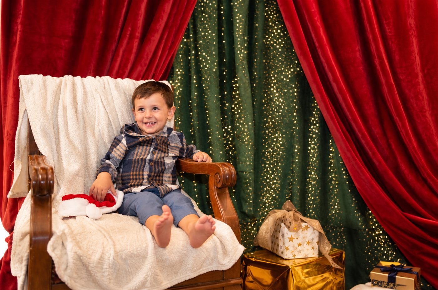 Niño sonriendo en el sillón clásico con cortinas rojas y regalos dorados