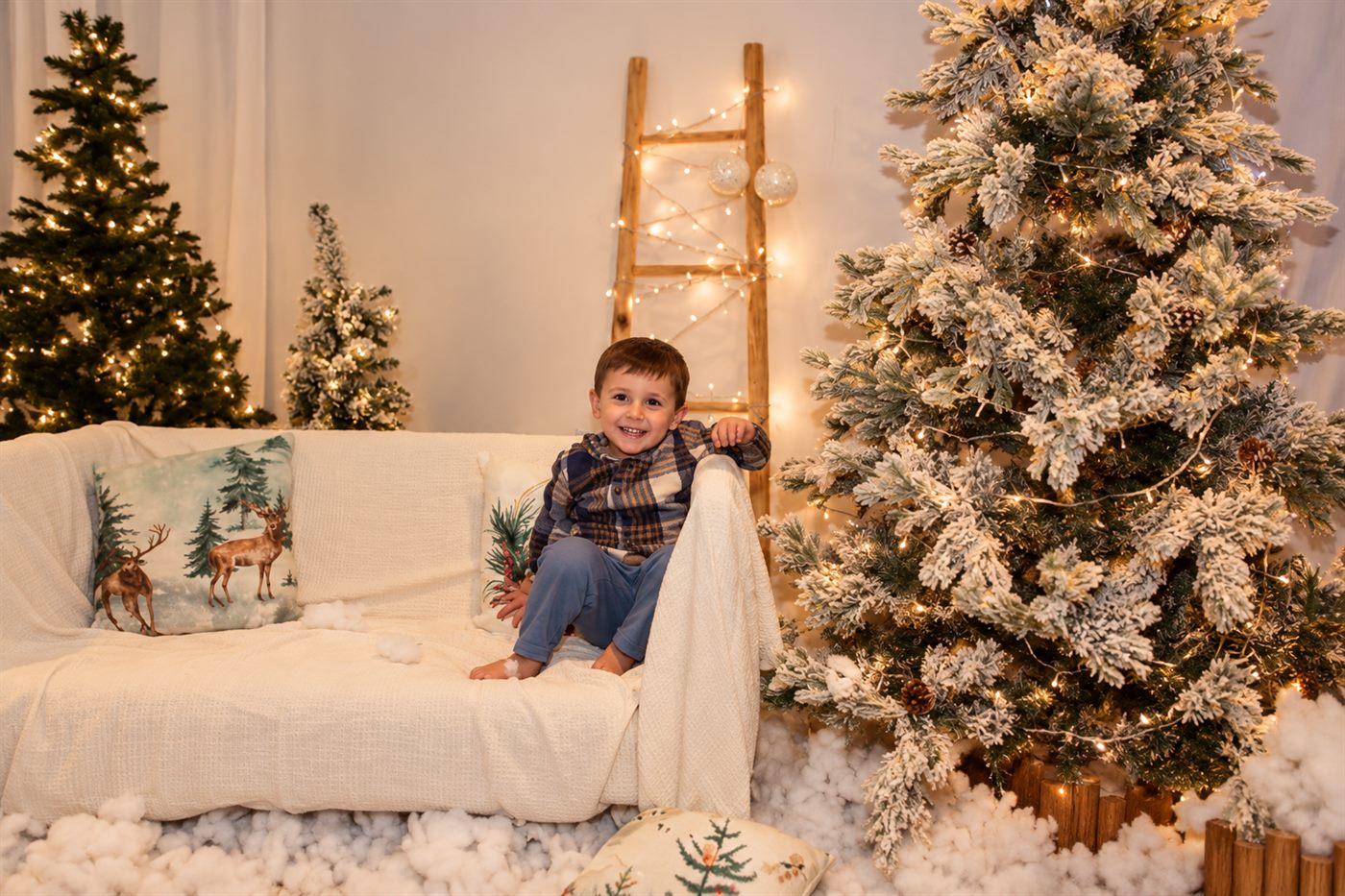 Niño sentado en el sofá blanco del escenario navideño junto al abeto nevado