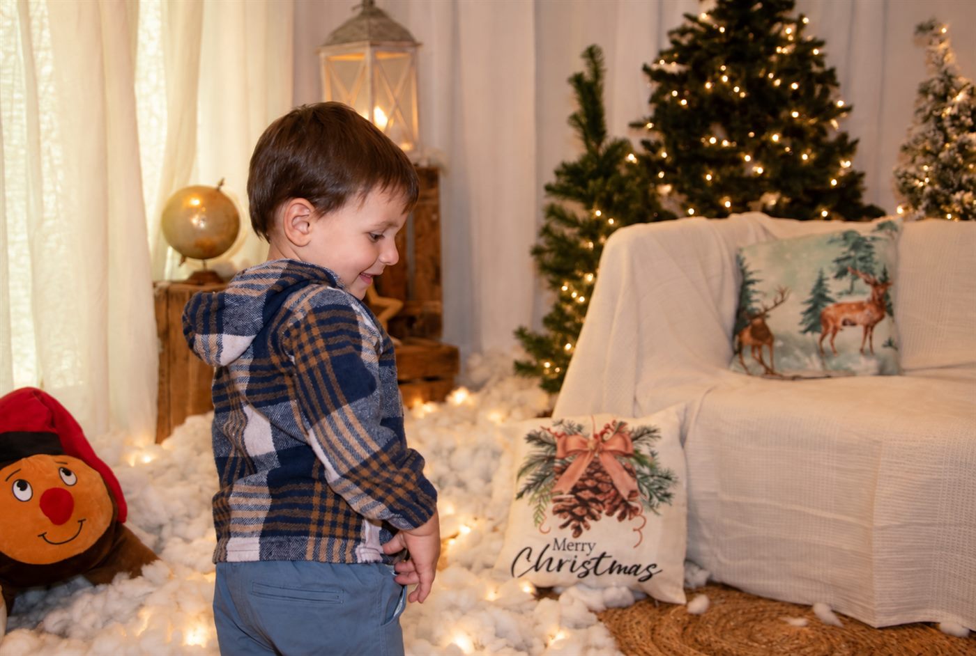 Niño sonriendo con el Tió en brazos delante del abeto iluminado
