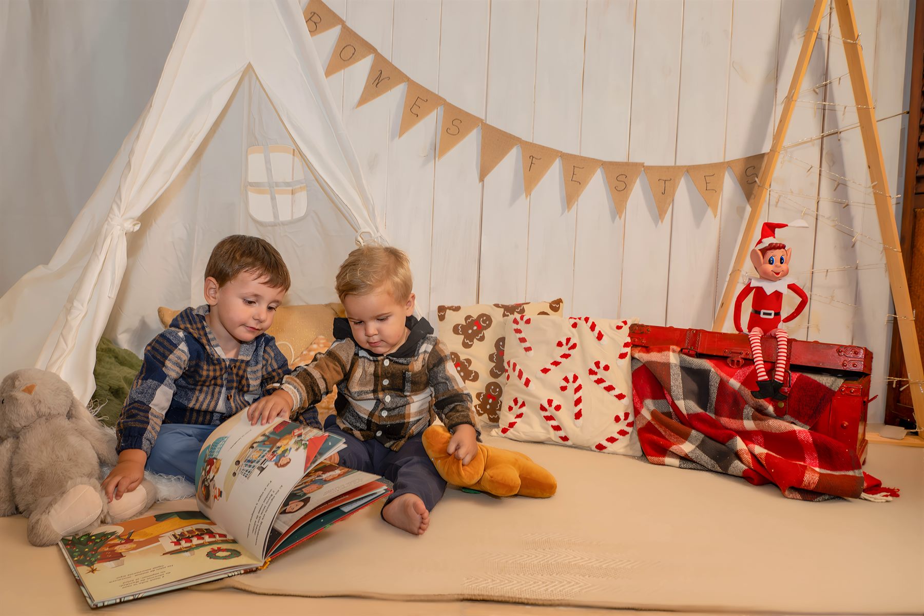 Dos hermanos leyendo un cuento delante de la tienda tipi, con cojines navideños y el elfo